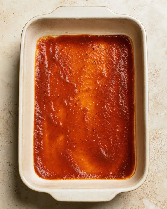 Salsa de enchilada extendida en el fondo de una fuente para horno