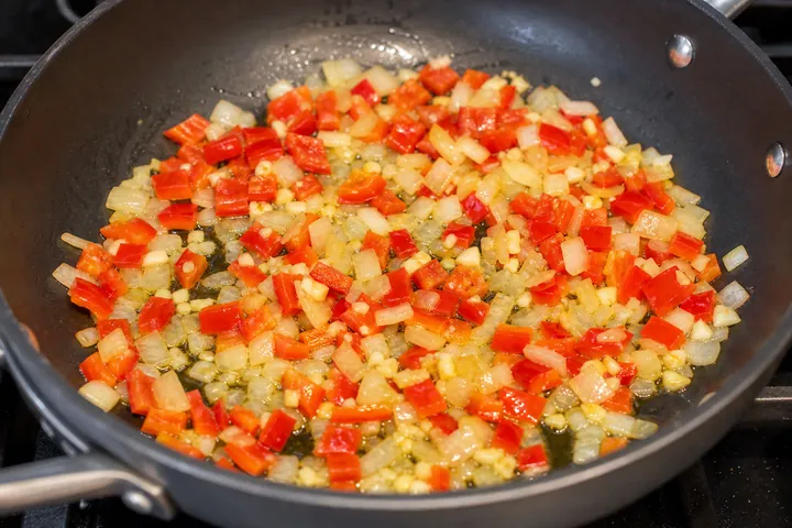 Onion, peppers, and garlic sautéing in a frying pan