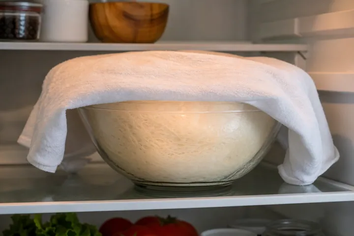 Brioche dough covered with a damp towel resting in refrigerator