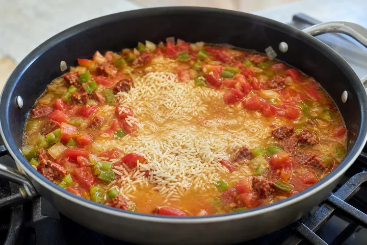 Arroz y tomates cociéndose con pimientos y chorizo en una sartén