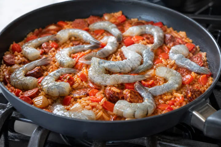 Gambas crudas colocadas sobre arroz con tomate casi hecho