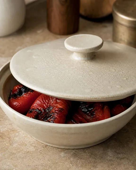 Charred peppers cooling in a covered bowl