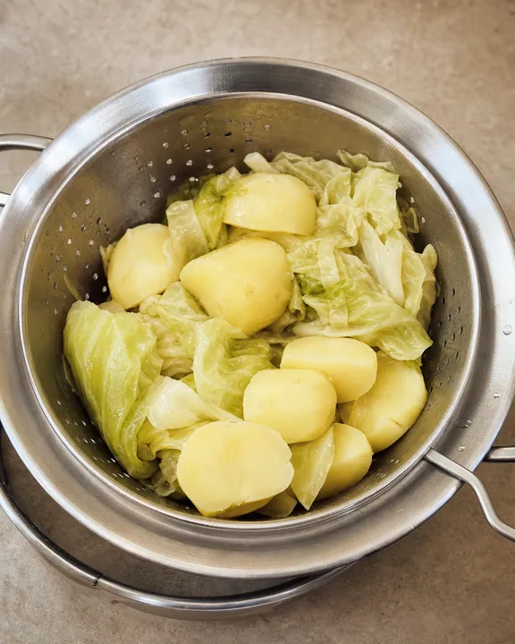 Col y patatas cocidas escurriendo en un colador