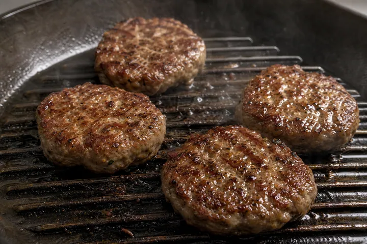 Lamb burger patties brushed with oil and grilling on a ridged pan