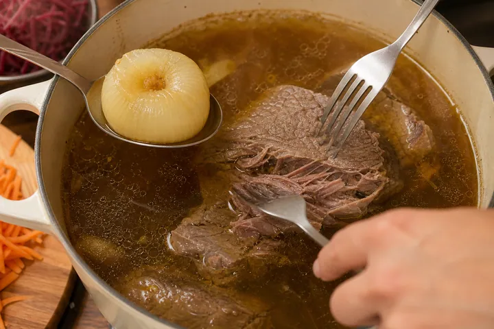 Tender beef pulled apart in broth while cooked onion is removed