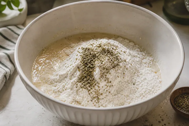 Flour and dried oregano added to a dough bowl