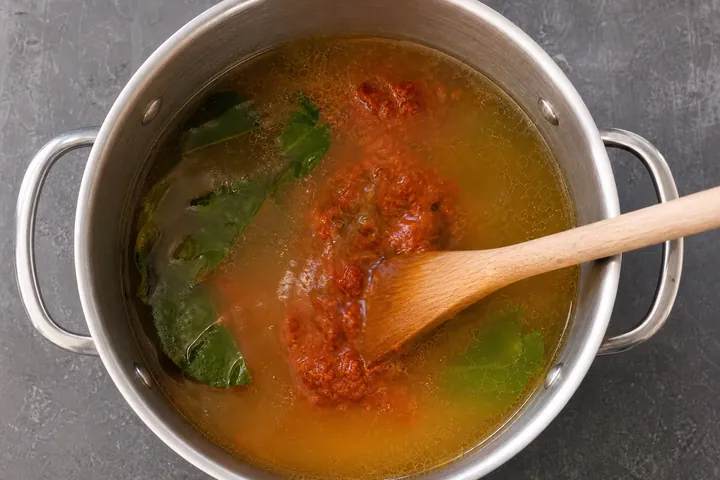 Stock, red curry paste, lime leaves, and fish sauce mixing in a pot