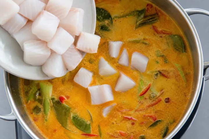 White fish cubes being added to simmering Thai curry broth