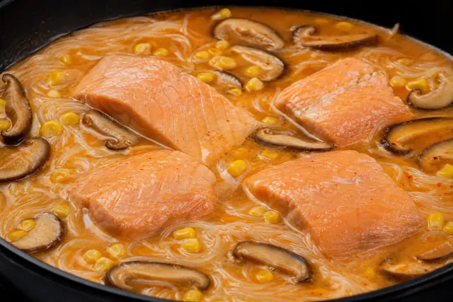 Filetes de salmón cocinándose en sopa de fideos con setas y maíz