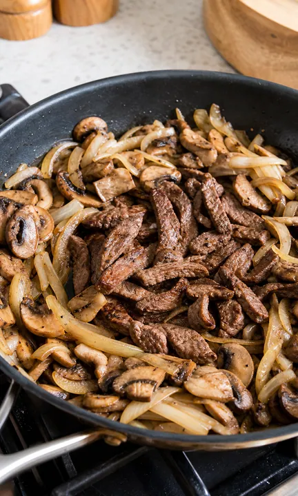 Carne de res chamuscada con champiñones y cebollas regresa a la sartén para hacer stroganoff