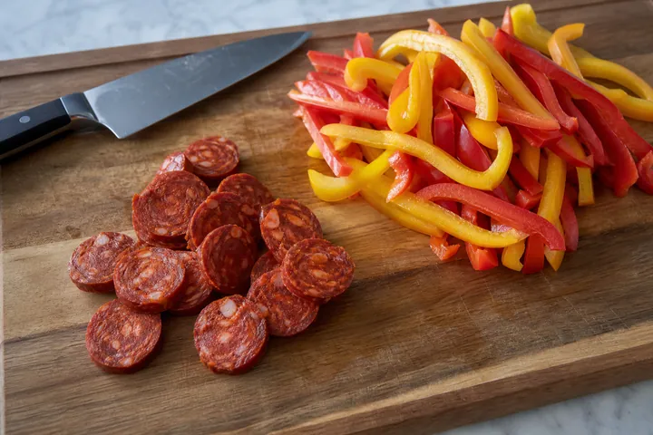 Sliced chorizo and thin bell pepper strips on a cutting board