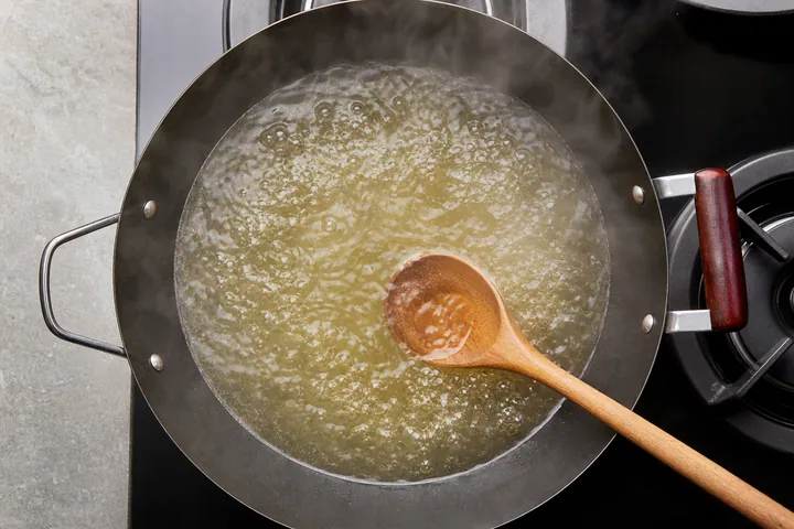 El caldo de pollo se hierve suavemente en un wok con una cuchara de madera.