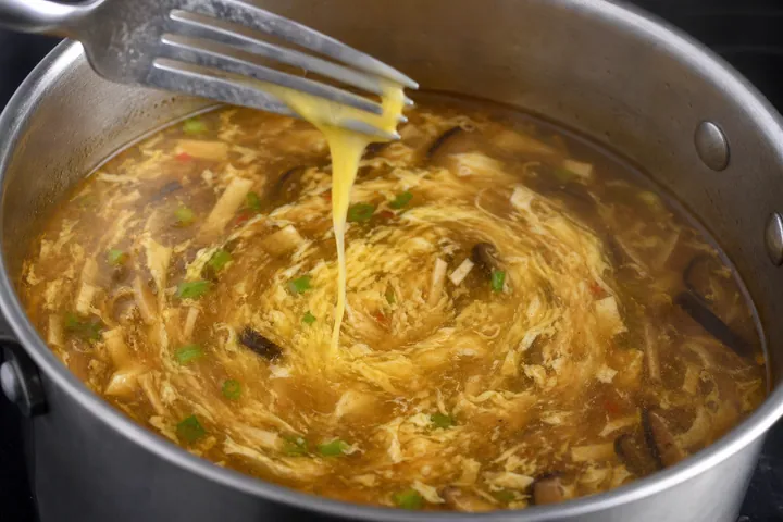 Huevo batido rociado con un tenedor sobre la sopa para hacer delicadas cintas de huevo