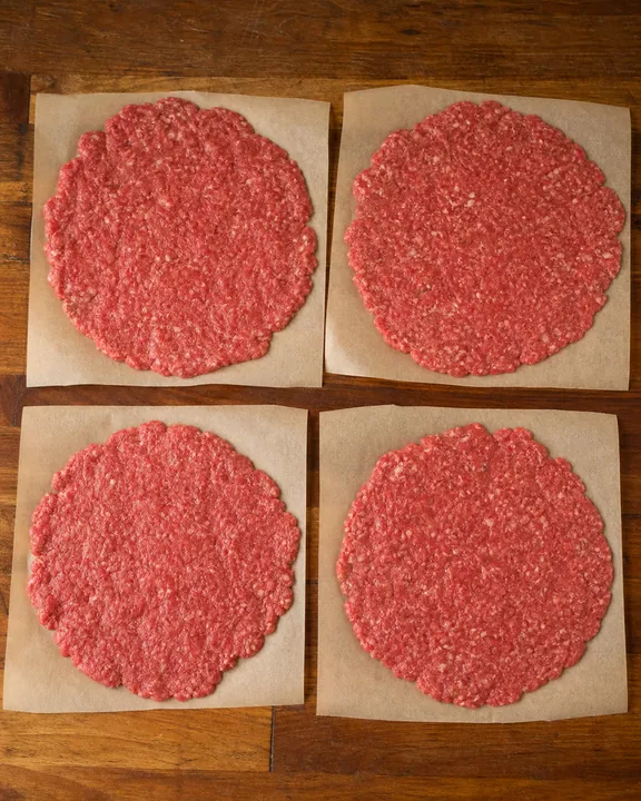 Thin beef patties on squares of parchment paper