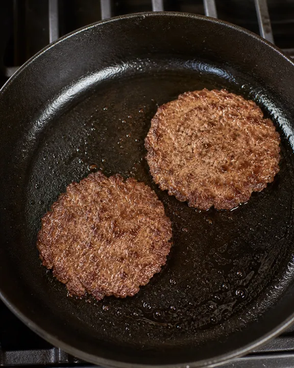 Two thin beef patties searing in a skillet