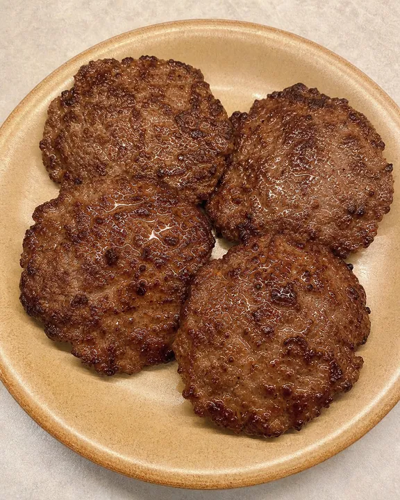 Four cooked beef patties kept warm on a plate