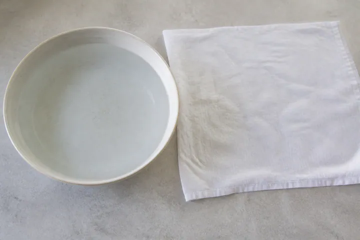 Un recipiente con agua tibia y un paño de cocina húmedo listo para enrollar.