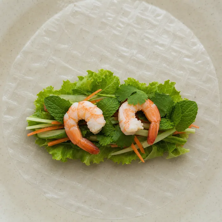 Menta, cilantro, dos gambas y verduras crujientes dispuestas en el centro de una lámina de arroz