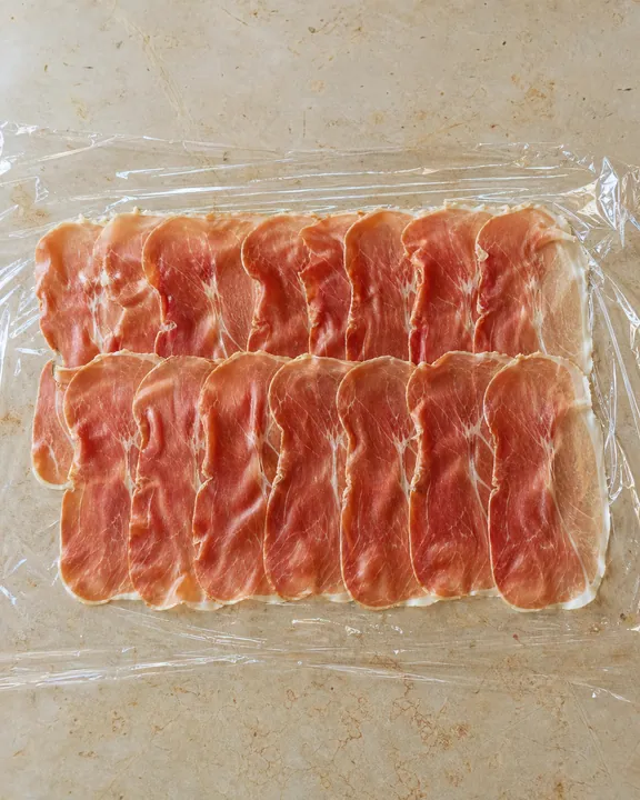 Overlapping Parma ham slices on plastic wrap