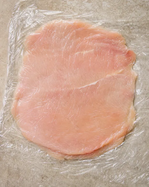 Pechuga de pollo aplanada entre láminas de film transparente