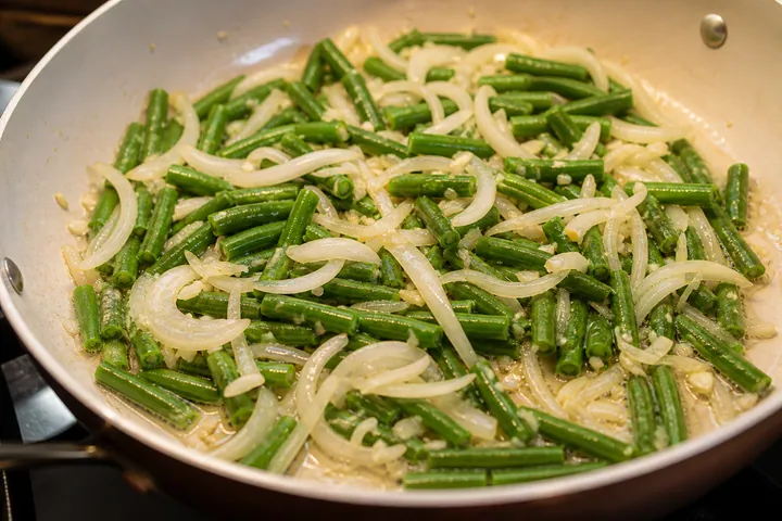 Green beans and sliced onion sautéing with minced garlic in butter